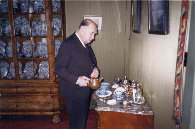 5. Jan Menze van Diepen pouring tea in his home in Haren with a well-stocked porcelain cabinet in the background, 1994