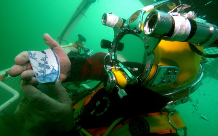 A diver in a diver lift returning to the surface shows a piece of porcelain from the wreck of the VOC ship Rooswijk. Photo #Rooswijk1740 project